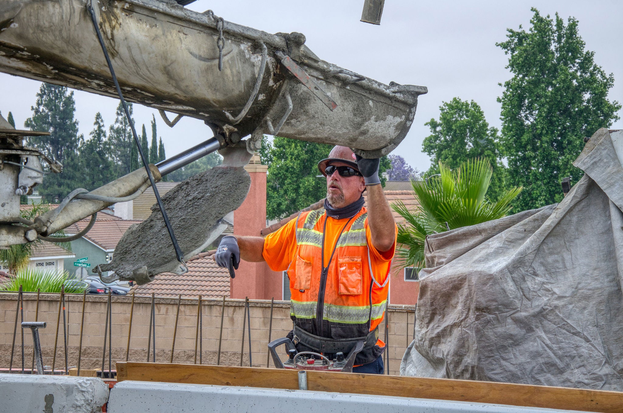 A construction worker in a safety vest and gloves guides wet concrete from a chute at a residential construction site.