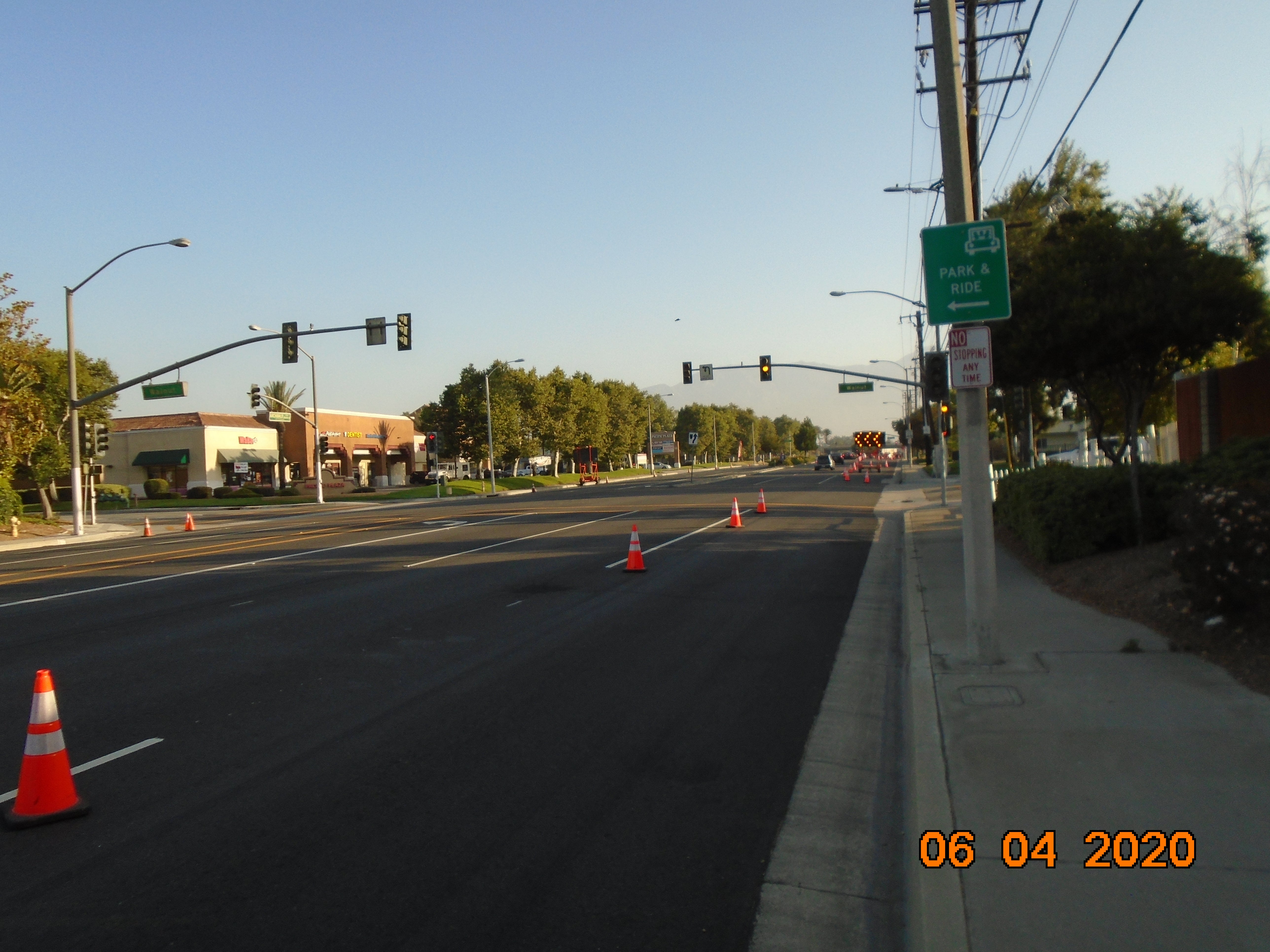 A city street with traffic cones marking the lanes and a Park & Ride sign on the sidewalk; traffic lights and businesses are visible in the background.
