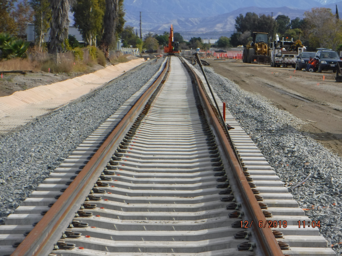 Newly constructed railroad tracks extending into the distance, with construction equipment and vehicles visible on the right side of the tracks.