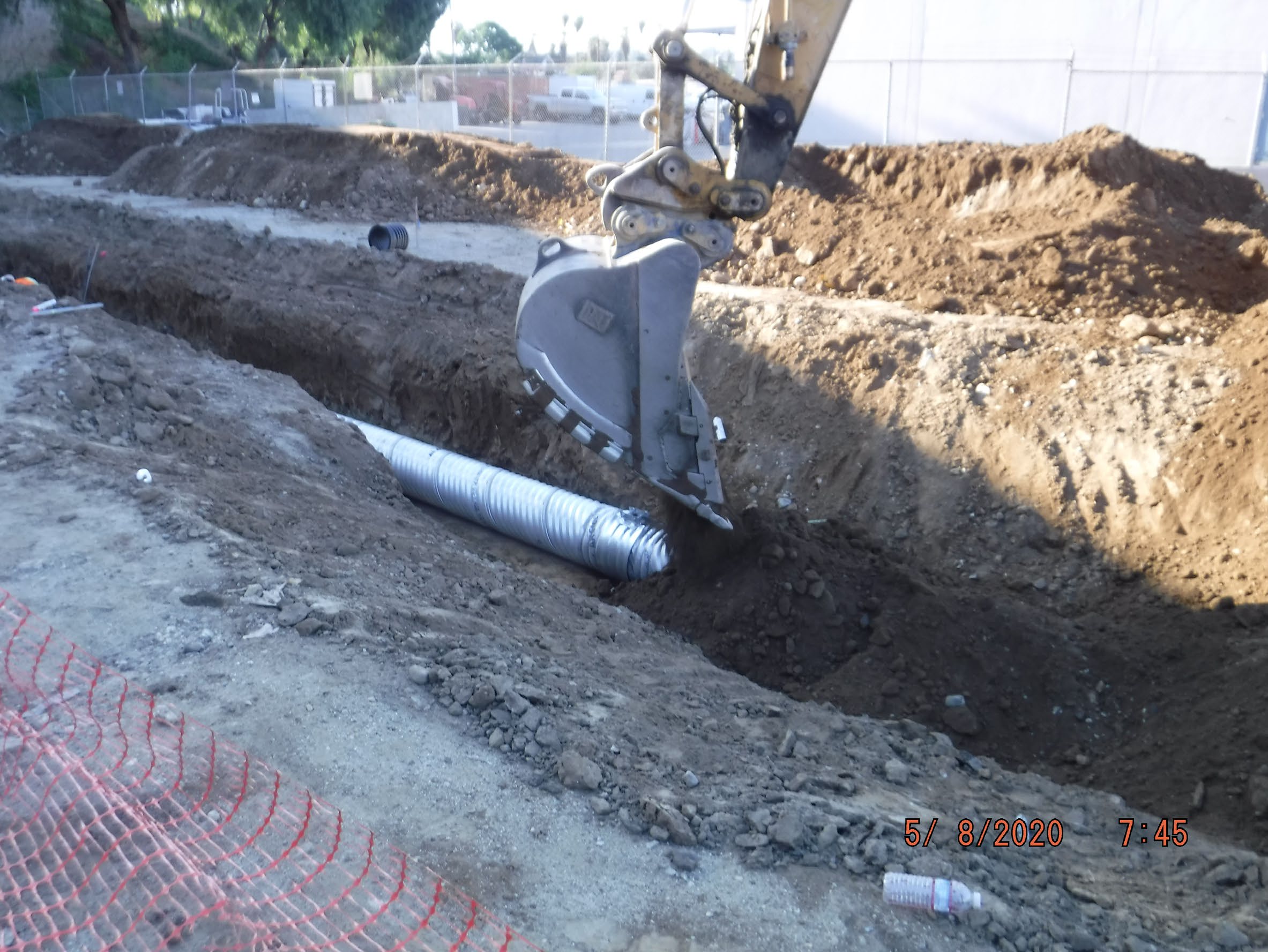 Excavator bucket digging near a partially buried corrugated metal pipe in a construction trench at a building site.