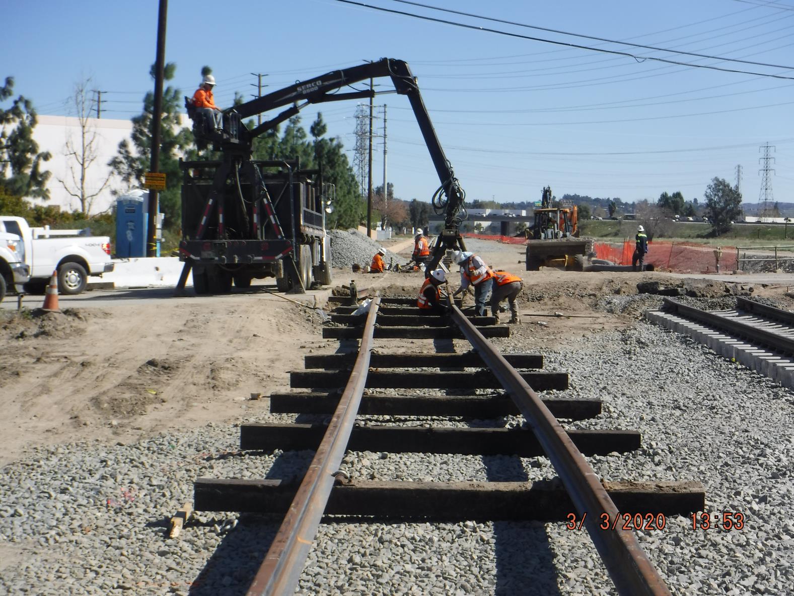 Construction workers in safety gear install and adjust railroad tracks using machinery and tools at an outdoor worksite.