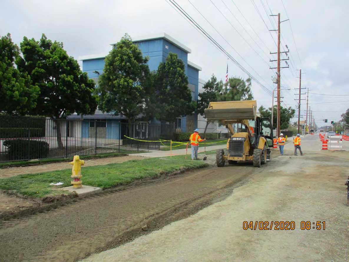 Construction workers operate machinery and work on a road near a building, with caution tape, traffic cones, and a fire hydrant visible.