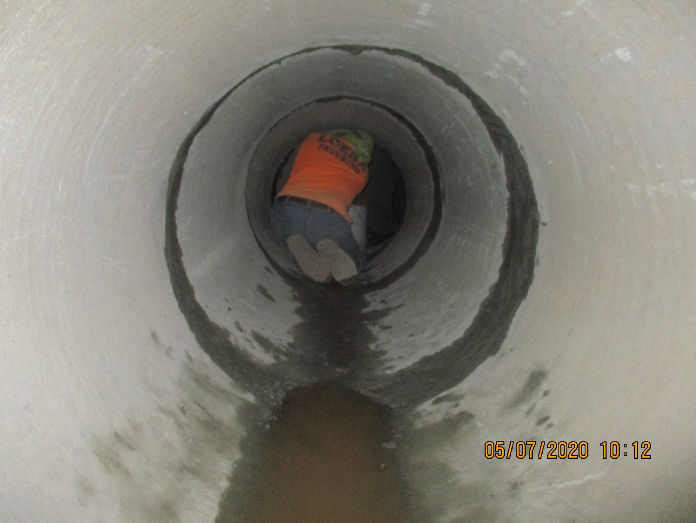 A person in an orange vest kneels inside a large concrete pipe tunnel, facing away from the camera. The date on the image reads 05/07/2020 at 10:12.