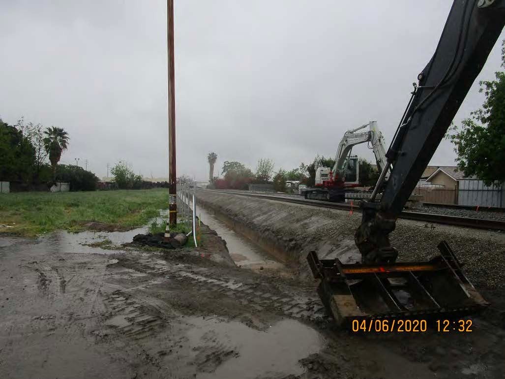 A muddy construction site with excavators near a canal on a cloudy day; timestamp reads 04/06/2020 12:32.