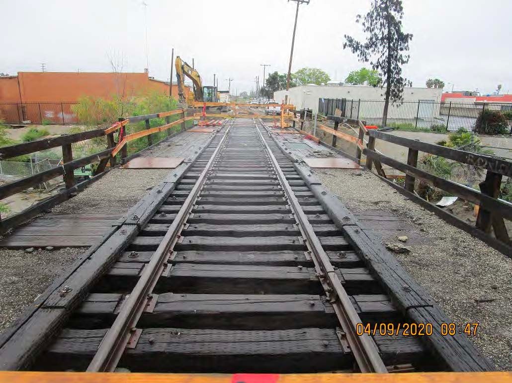 Railroad tracks on a wooden bridge under construction, with construction equipment and barriers visible in the background. Photo dated April 9, 2020, at 8:47 AM.