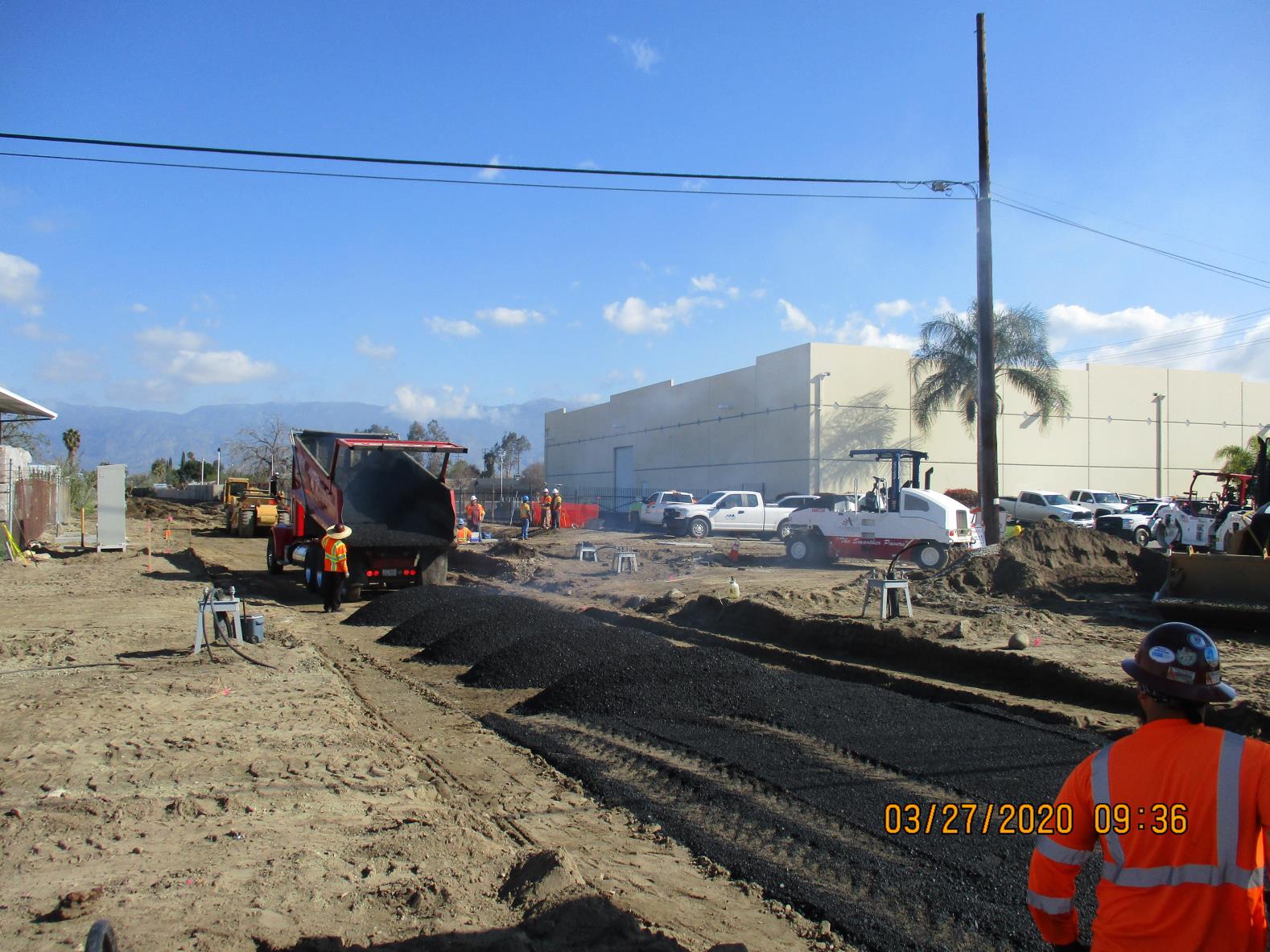Construction workers are paving a road with asphalt at a construction site, using heavy machinery and wearing orange safety vests and helmets.