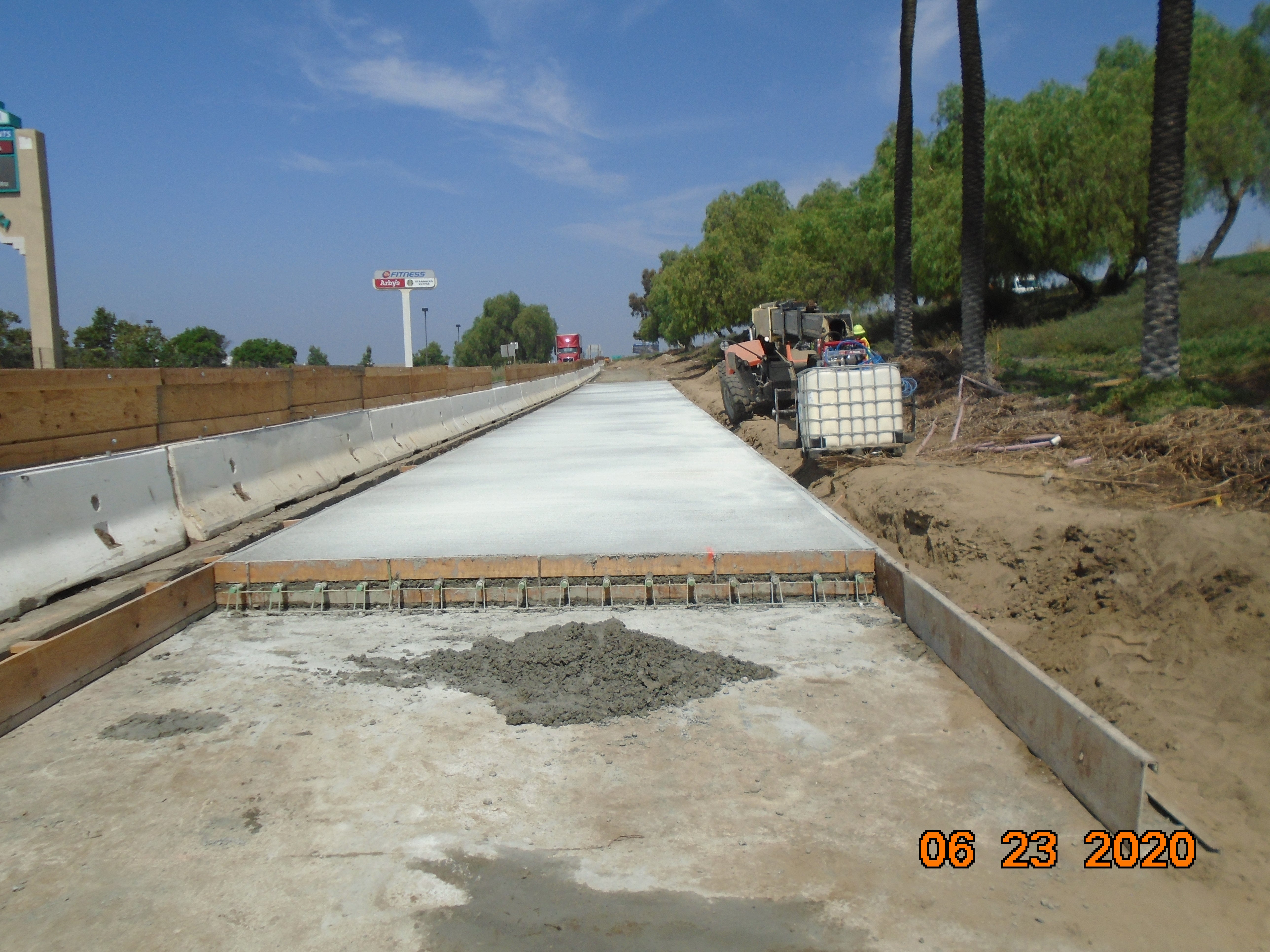 A newly poured concrete road section under construction with barriers and construction equipment visible; date stamp reads June 23, 2020.
