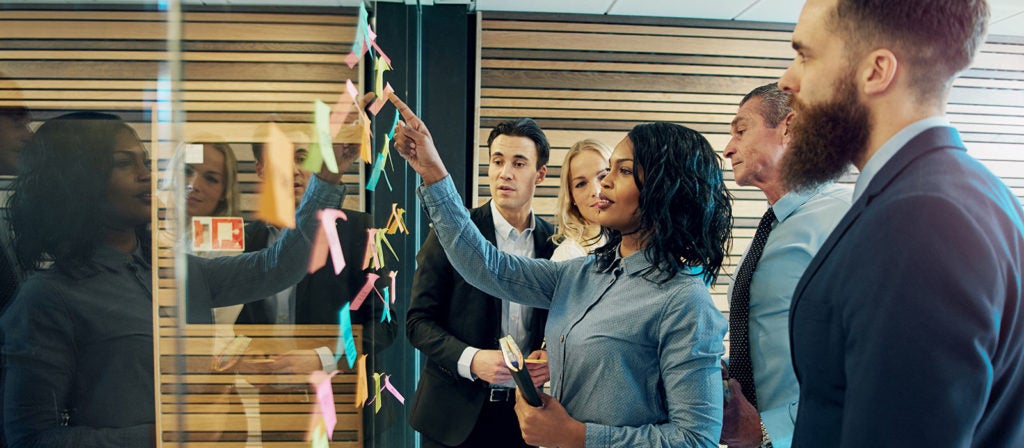 People standing in front of a board in a meeting room and reviewing post-it notes on the board