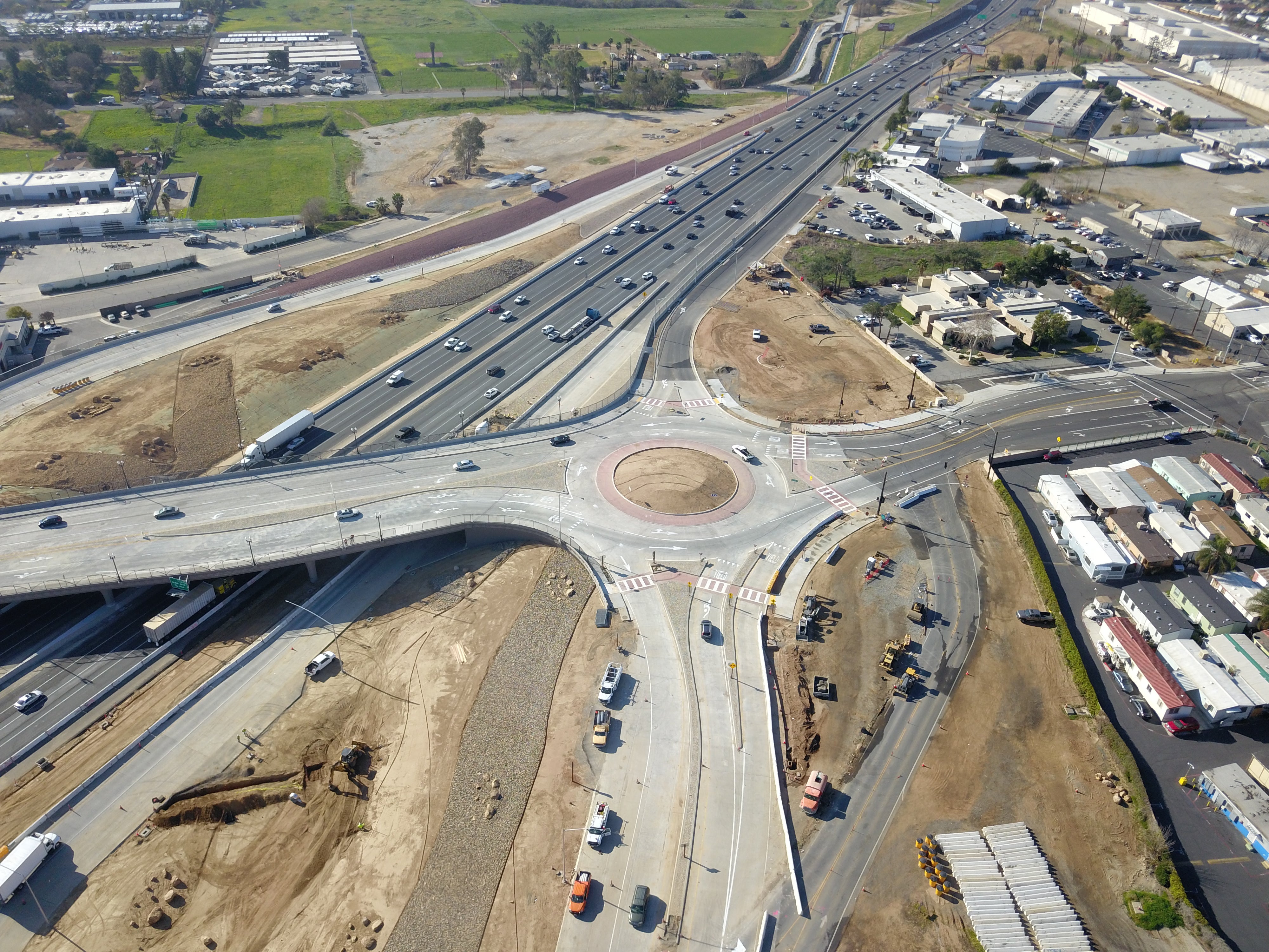 Aerial view of a large roundabout interchange connecting multiple roads and highways, with vehicles visible on the roads and surrounding industrial and residential areas.