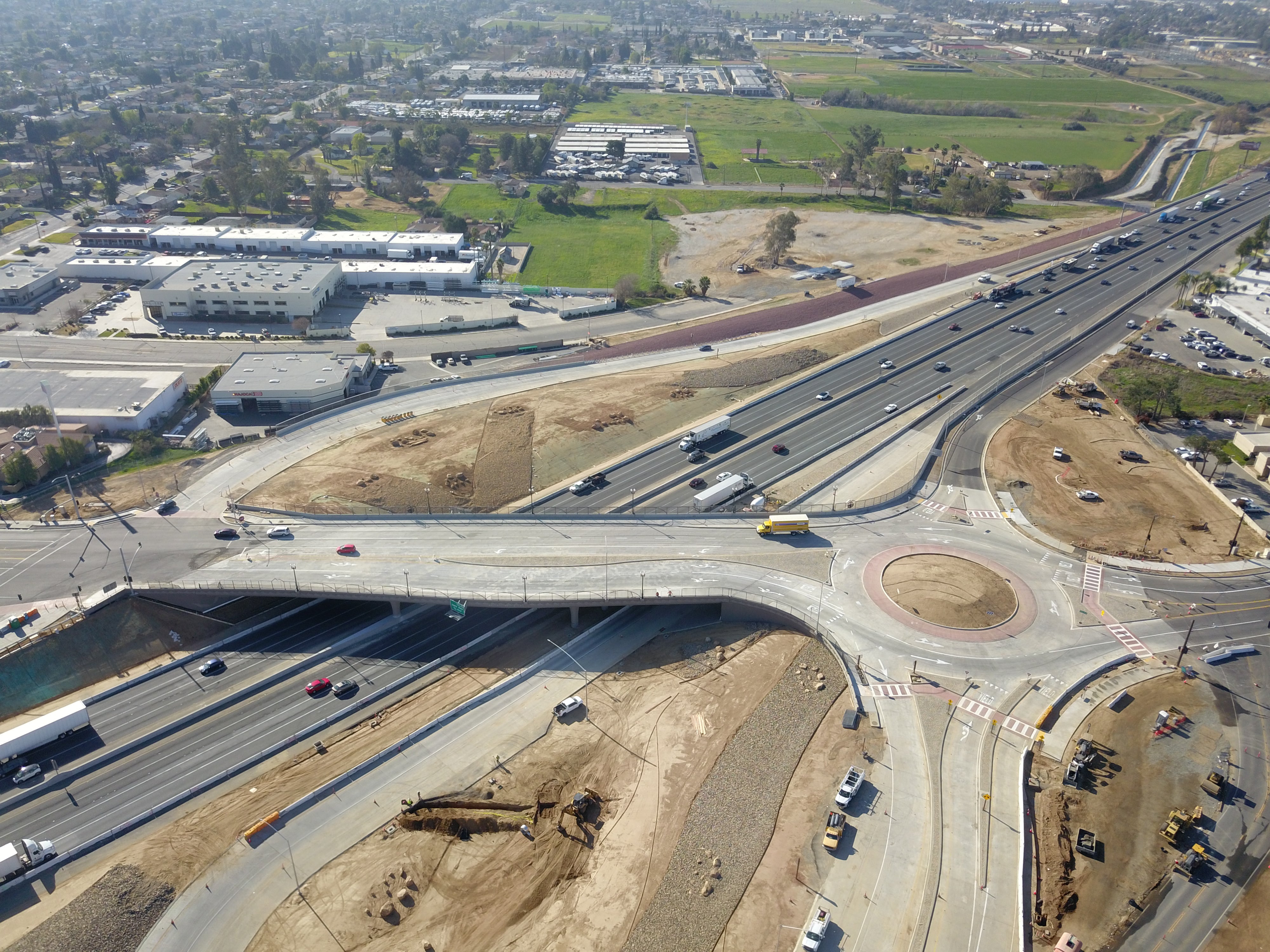 Aerial view of a highway interchange featuring a roundabout, multiple lanes, overpasses, and surrounding commercial and undeveloped land.