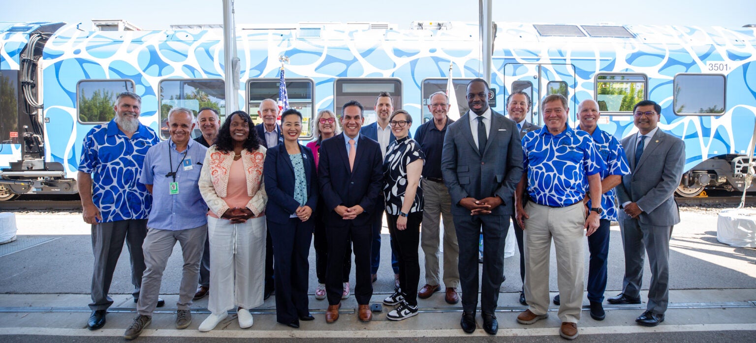 A group of people standing and smiling in front of a blue and white patterned train.
